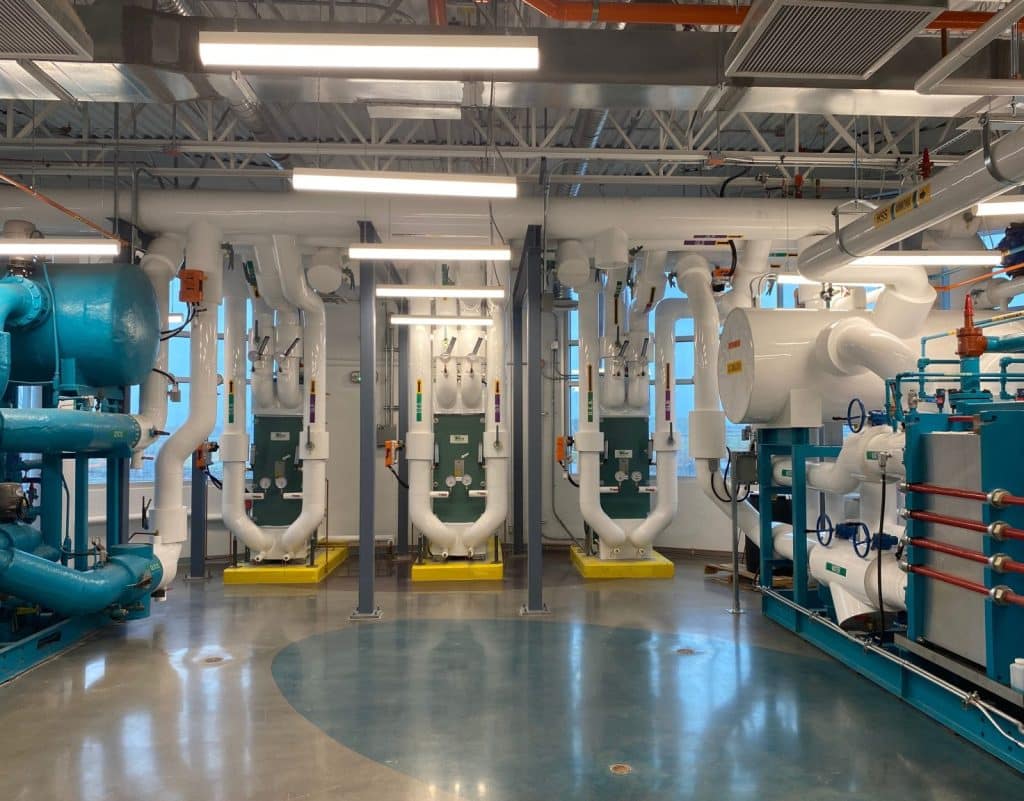 A large industrial room with teal and white pipes, machinery, and equipment, with a polished concrete floor.