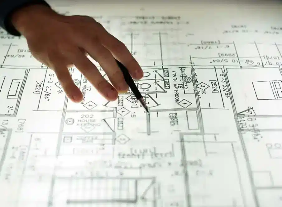 A person's hand with a pen points to a detailed architectural blueprint with "WOMEN WASHROOM" visible.