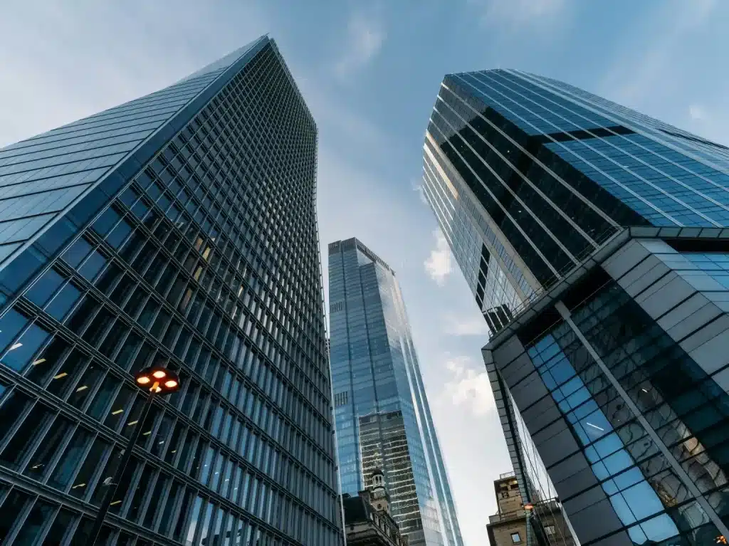 Three tall, modern glass skyscrapers reach towards a bright blue sky with scattered white clouds.
