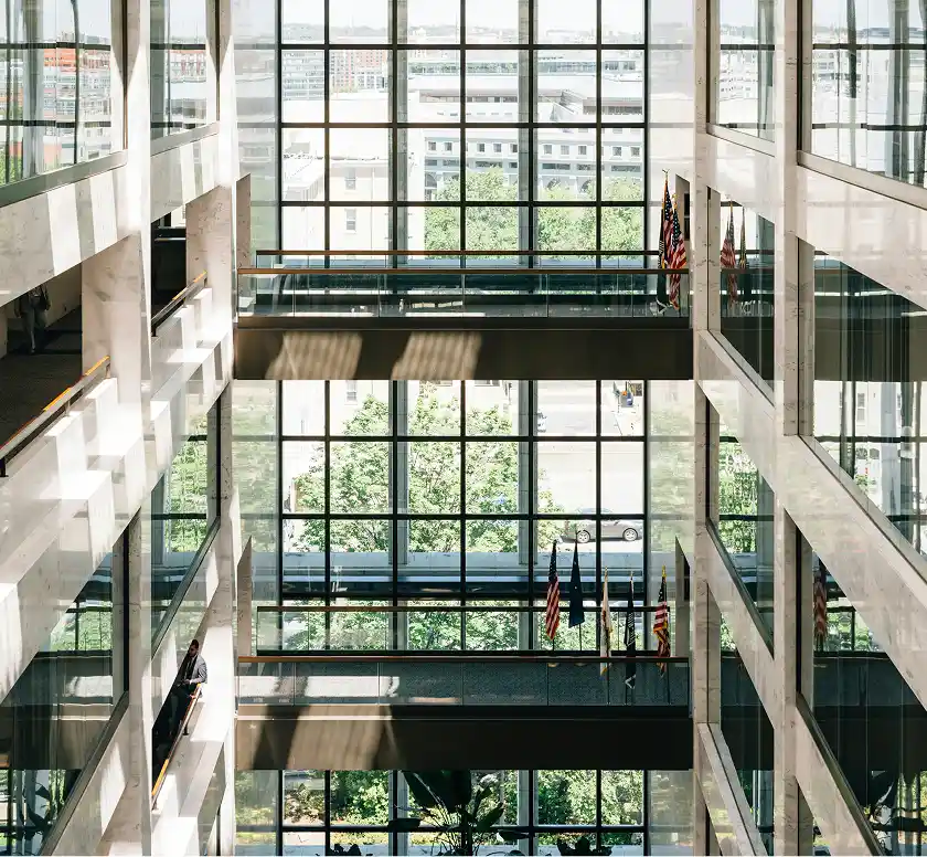 A multi-story building interior with large windows, balconies, and American flags hanging from a railing.