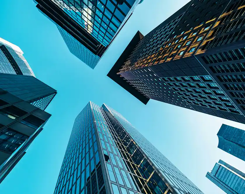 Looking up at several modern skyscrapers with reflective glass windows against a bright blue sky.