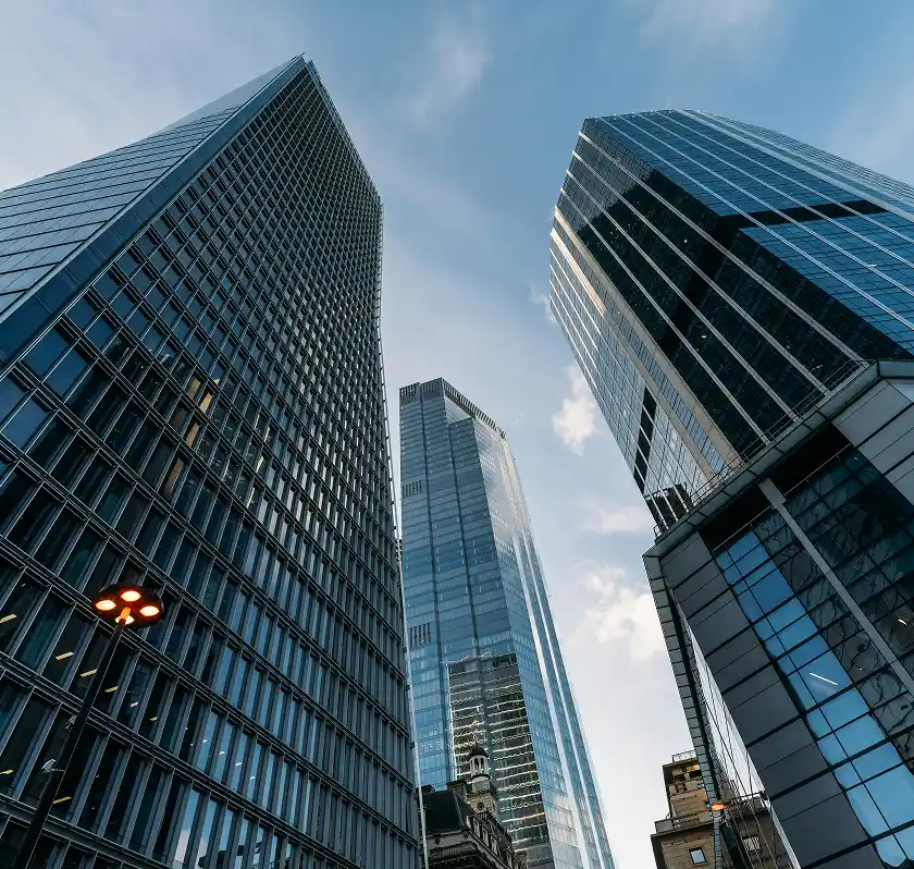 A low-angle view of three modern glass skyscrapers against a partly cloudy blue sky.